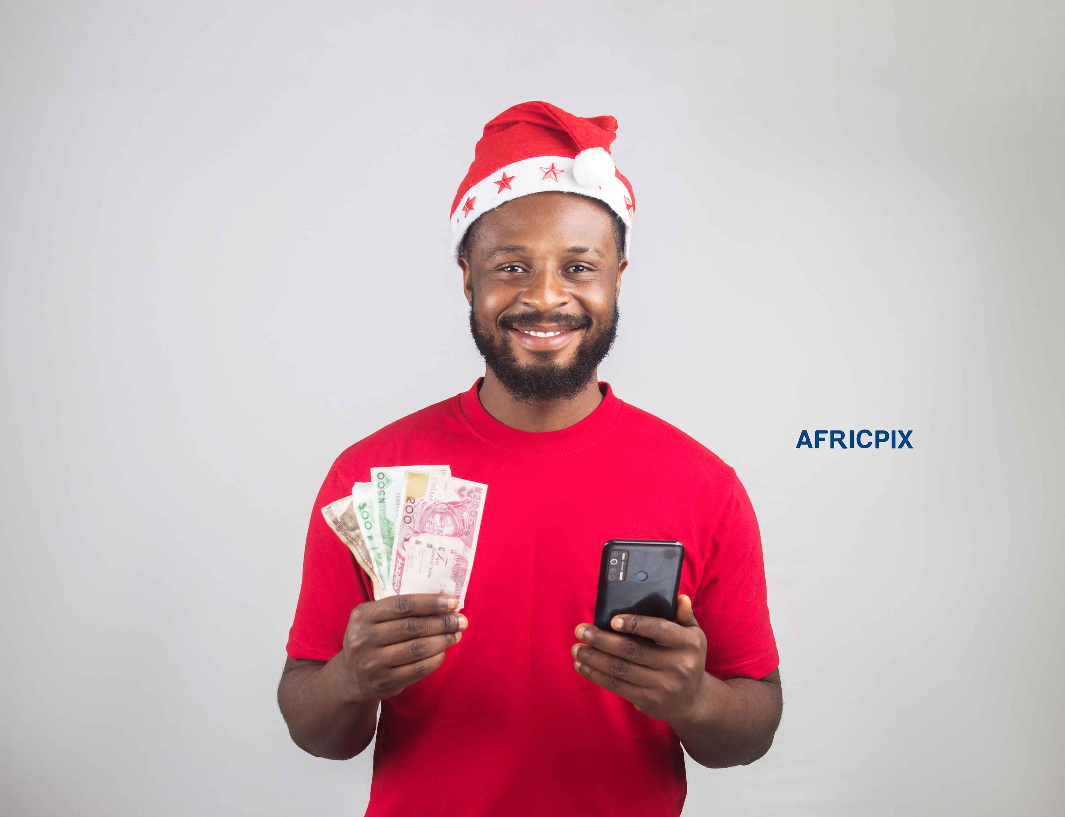 An African Nigerian man wearing a Christmas cap, holding Naira notes in one hand and a phone in the other. 2